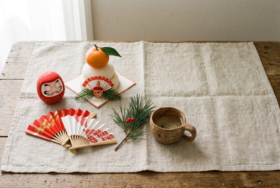Japanese New Year flat lay with daruma, kagami mochi, fans and pine on linen