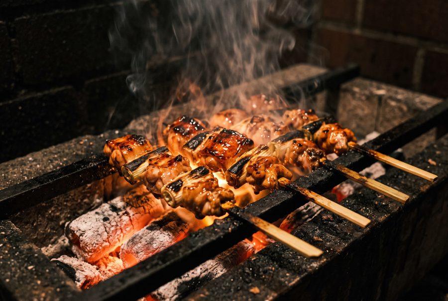 Yakitori chicken skewers grilling over charcoal with smoke and glaze