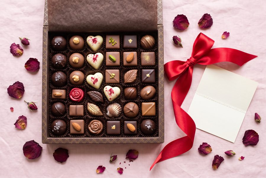 Open box of assorted chocolates with red ribbon and rose petals, Valentine top view