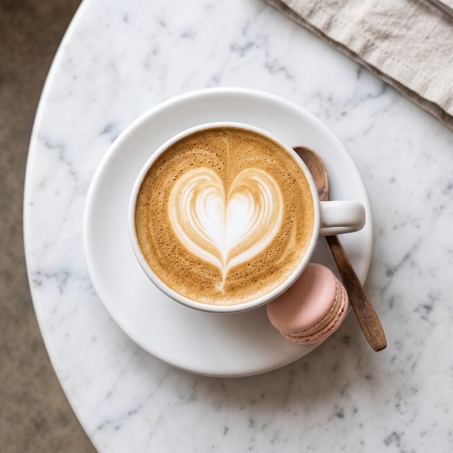 Latte with heart foam art and pink macaron on marble table, overhead